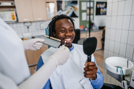 Handsome young black man choosing a shade of dental veneers at the dentist's office.